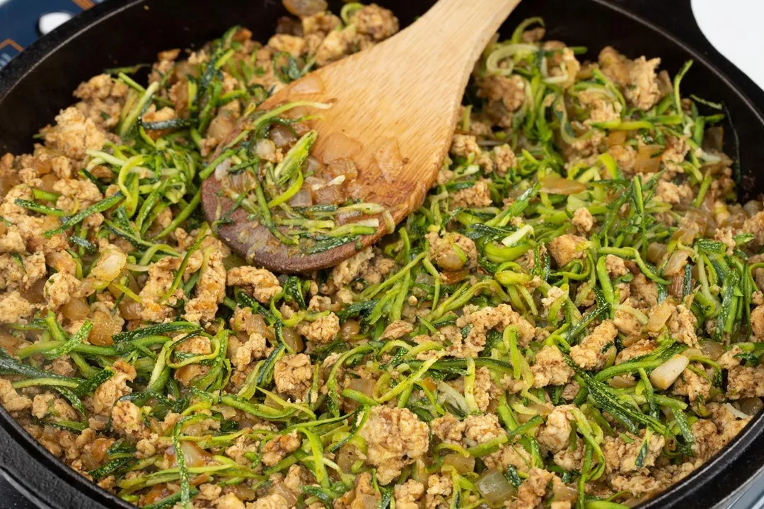 cooking ground chicken with grate zucchini in a skillet
