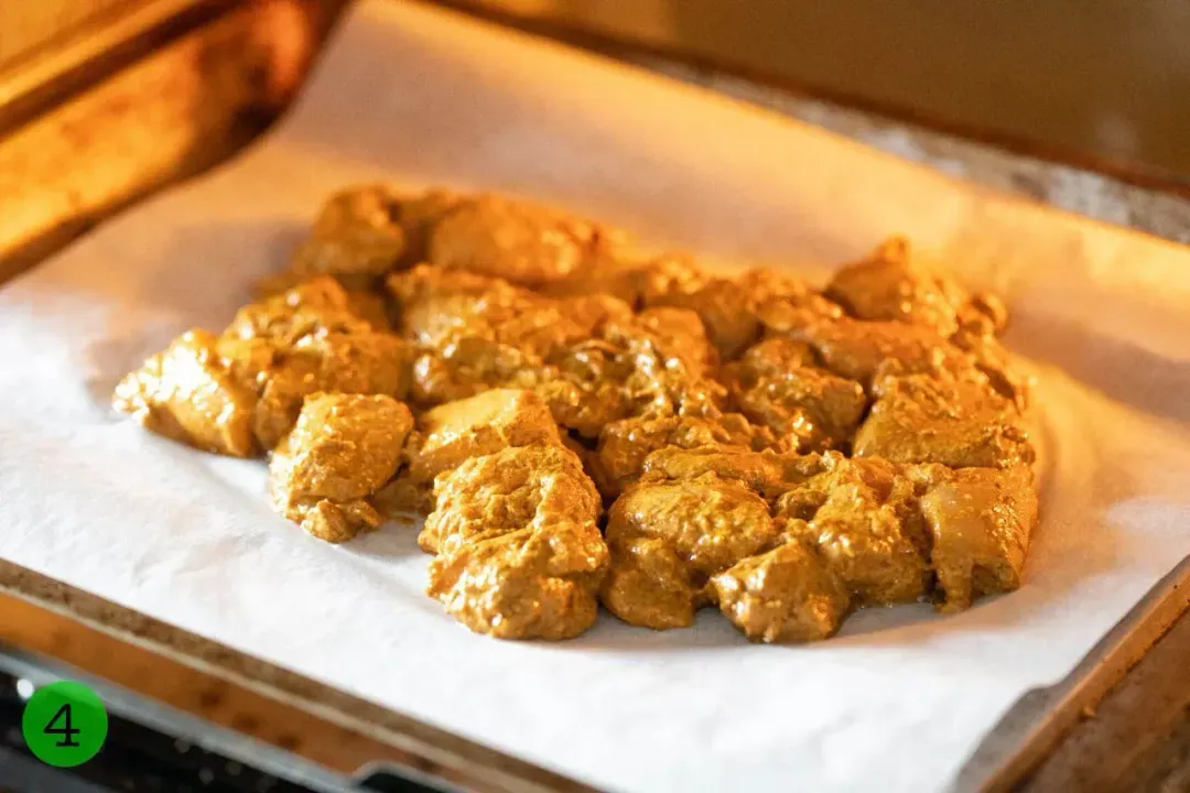 Chicken Tikka Masala laid on a sheetpan lined with parchment paper cooking in the oven