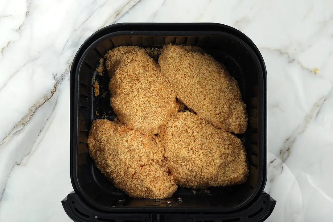 four coated chicken breasts in an air fryer basket