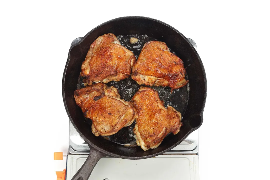 A large black skillet cooking four chicken thighs whose skin is evenly browned