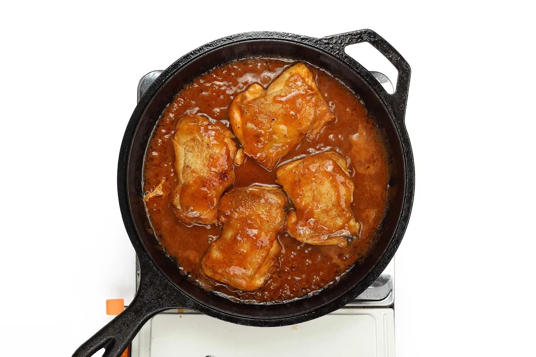 Four chicken thighs with Buffalo sauce in a skillet