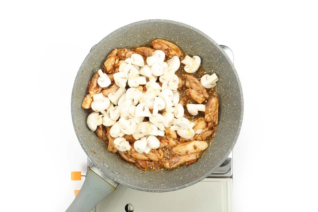 Chicken thighs and white mushrooms being cooked in a pan