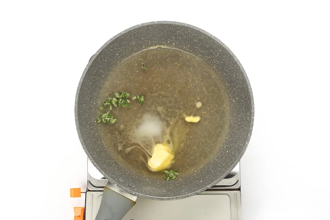 A large and deep pan cooking a butter cube and some chopped herbs with olive oil