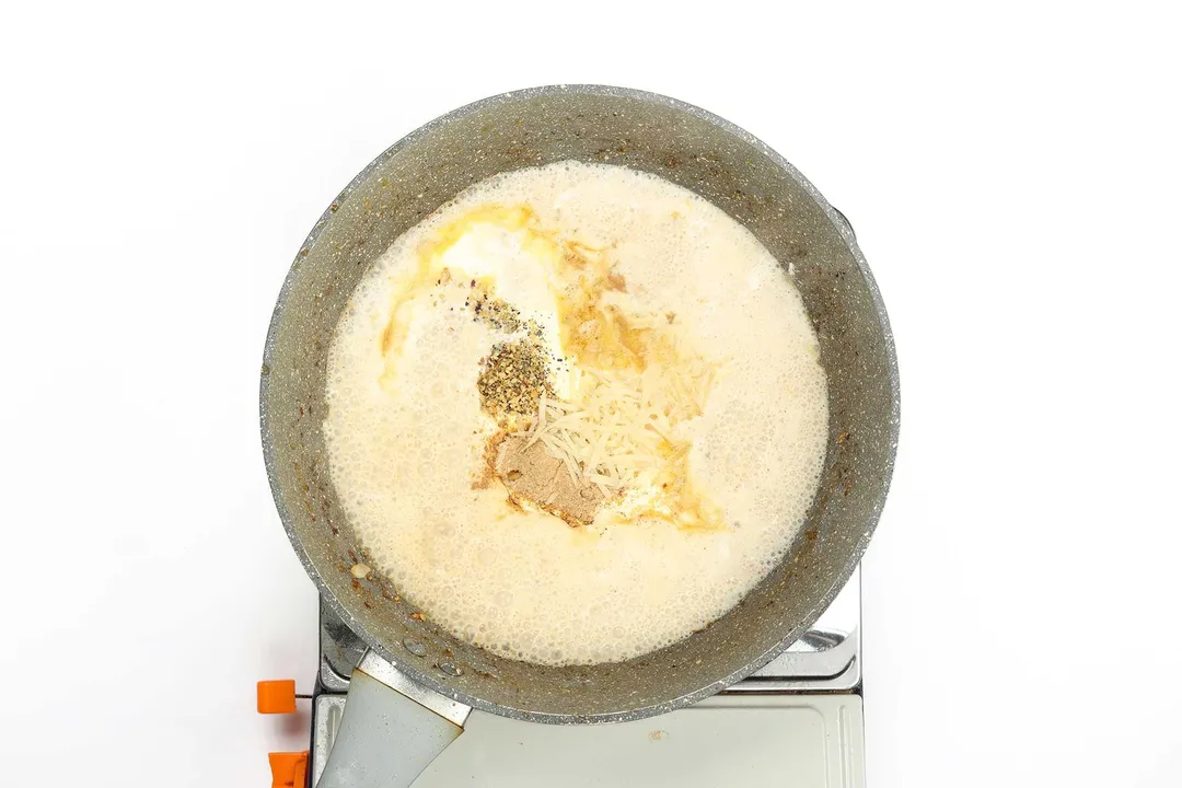 Whole milk, heavy cream, parmesan cheese, and seasonings being combined together in a pan