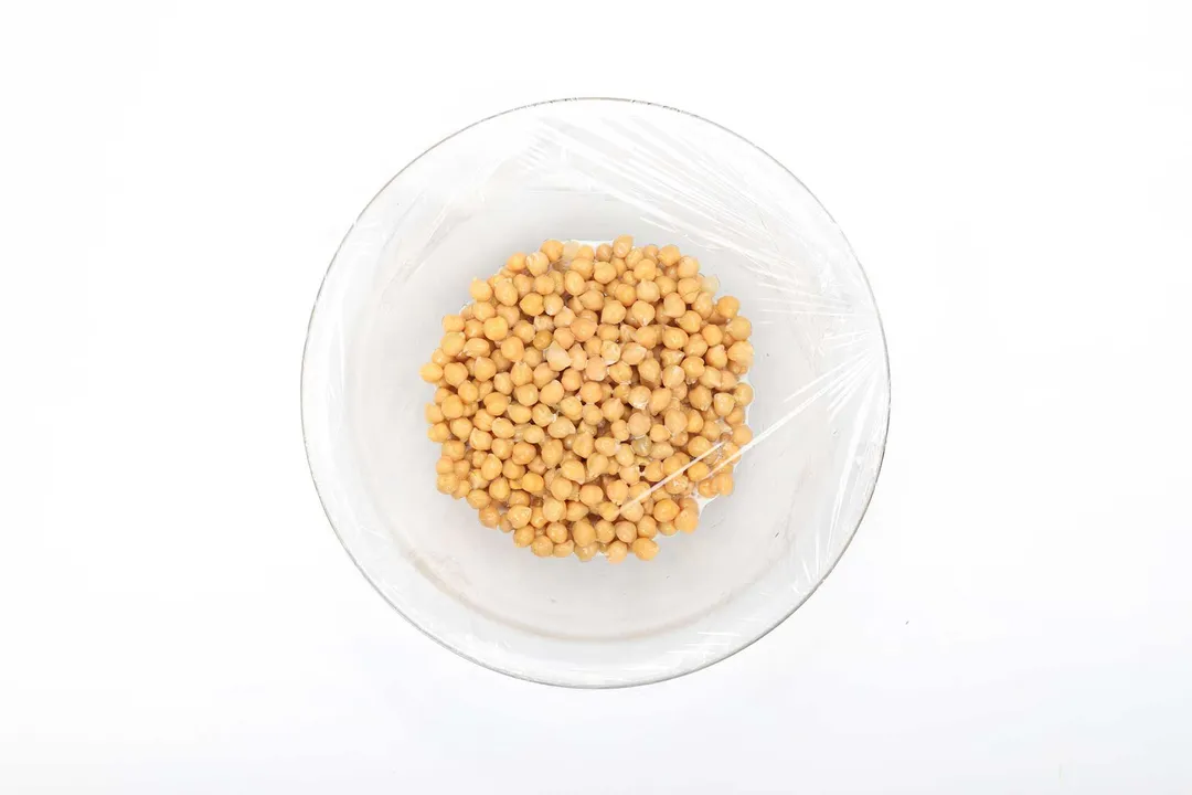 Chickpeas in a large bowl covered with plastic wrap