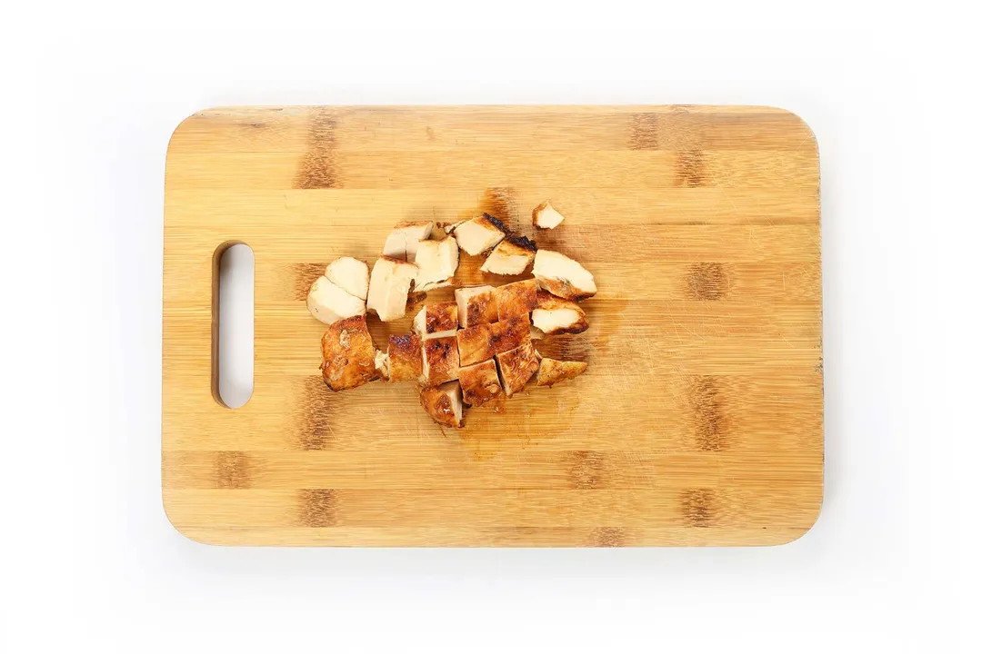 A rectangle chopping board with cooked chicken cubes laid on top