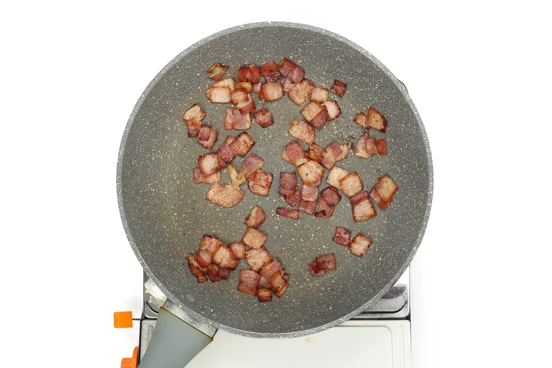 A large pan cooking small pieces of bacon