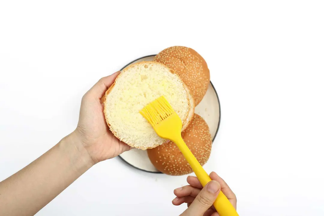 A hand sweeping butter onto the inside of a hamburger bun