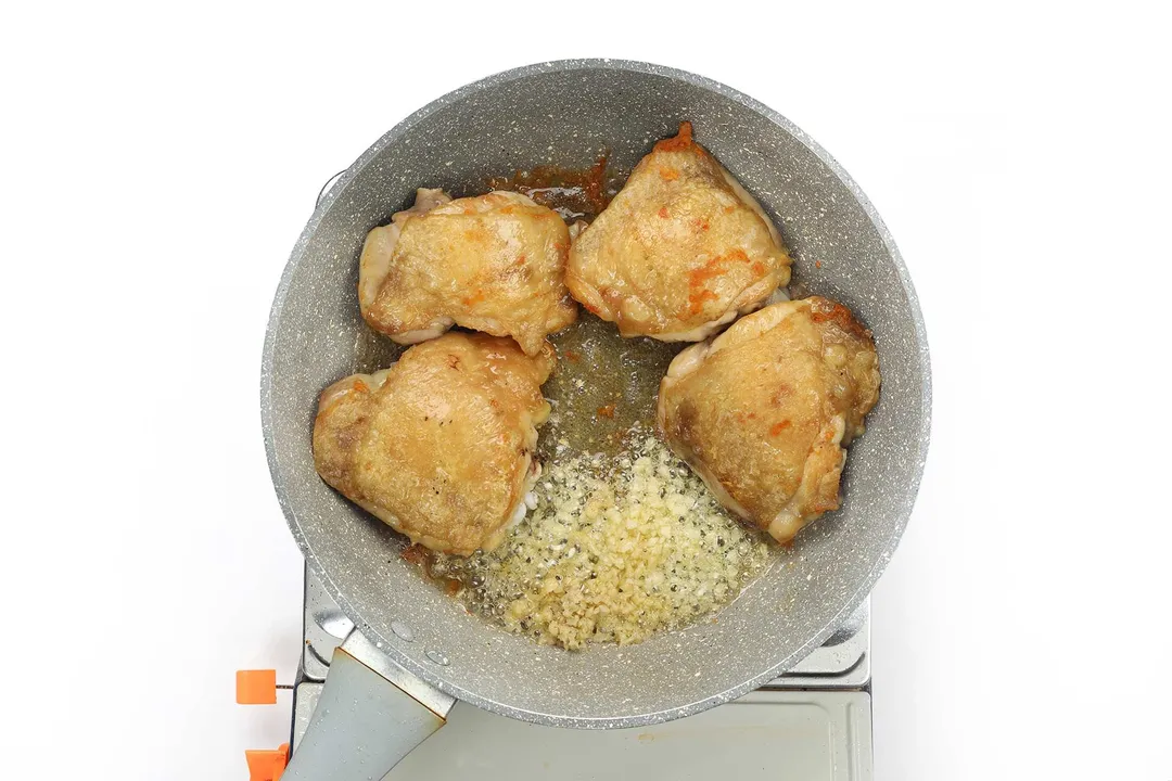A large pan cooking four pieces of chicken thighs with diced onion and minced garlic