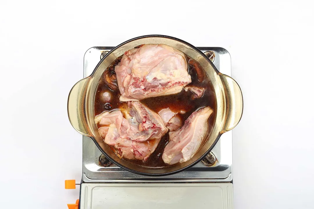 A saucepan cooking raw chicken thighs in a dark brown sauce