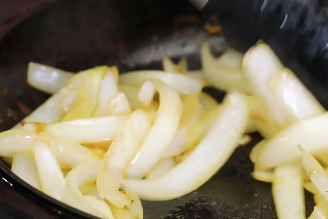 Sliced white onion sizzling and glistening in a black skillet