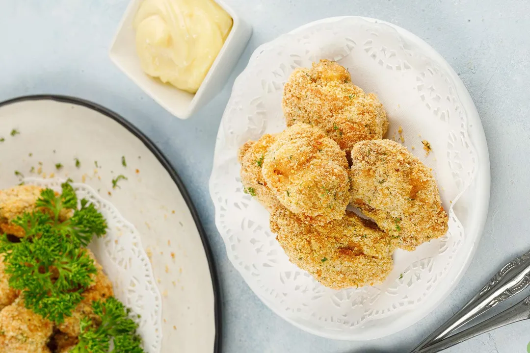 two plate of cooked chicken nuggets and a small bowl of mayonnaise