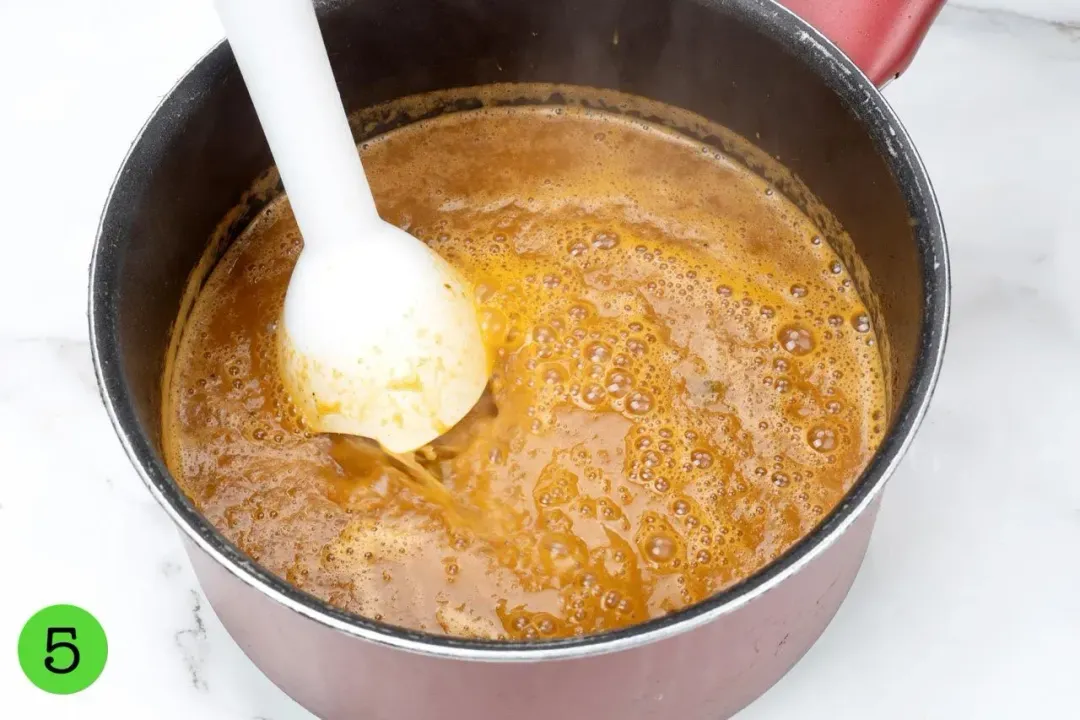 An immersion blender blending a soup in a pot