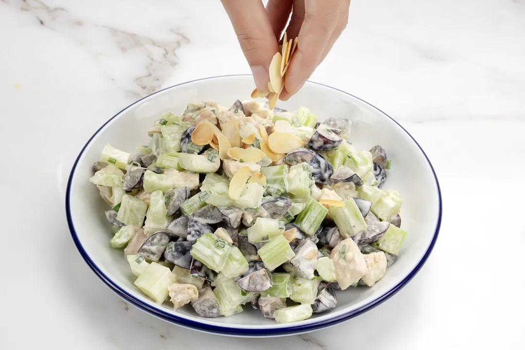 a hand sprinkle chopped almond on top of a salad plate