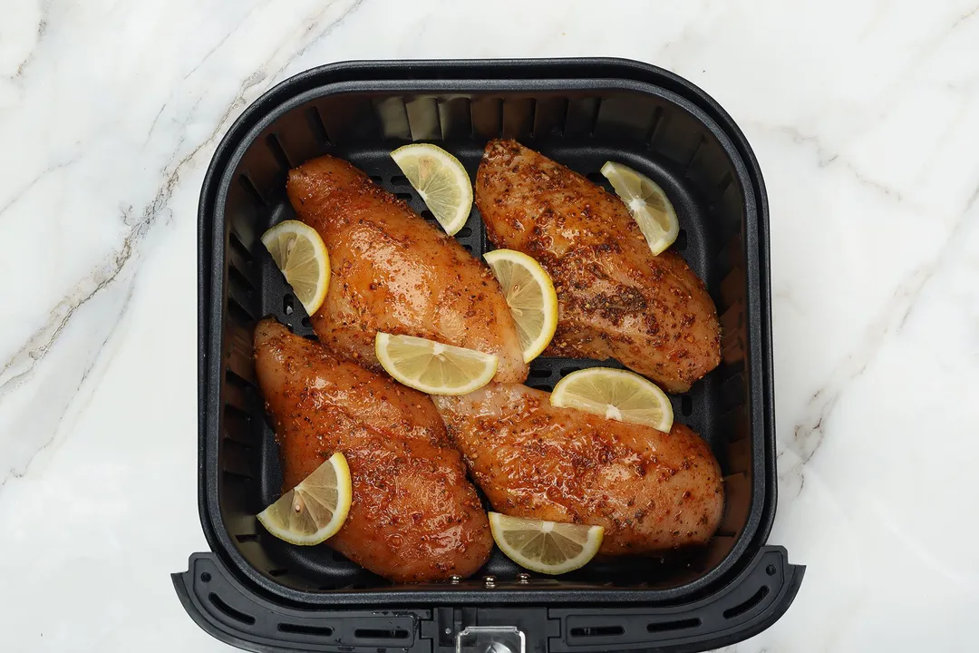 four chicken breasts and lemon slices in an air fryer basket