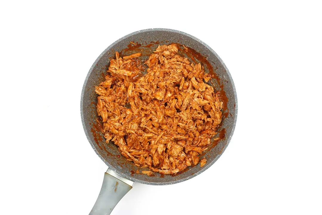 A large pan cooking shredded chicken covered in ketchup and spices