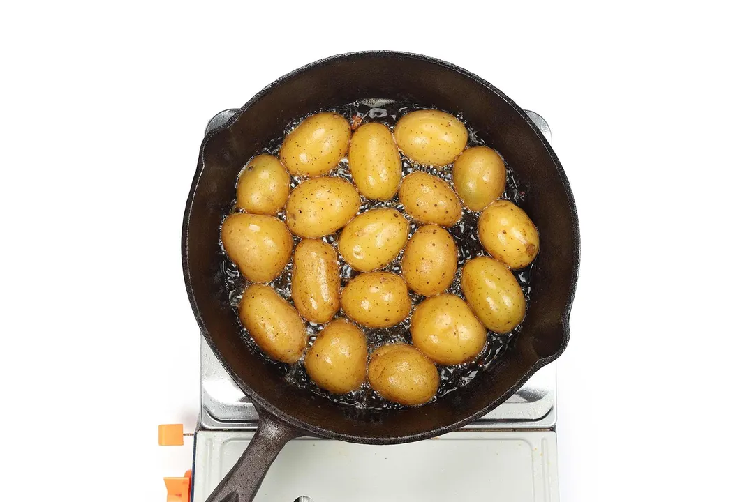 A large black skillet cooking baby potato halves laid upside down 
