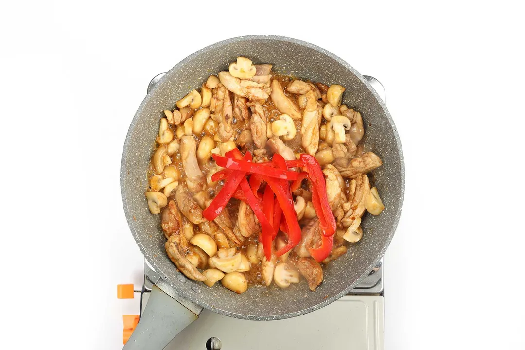 Chicken thighs, white mushrooms, and red bell peppers in a pan