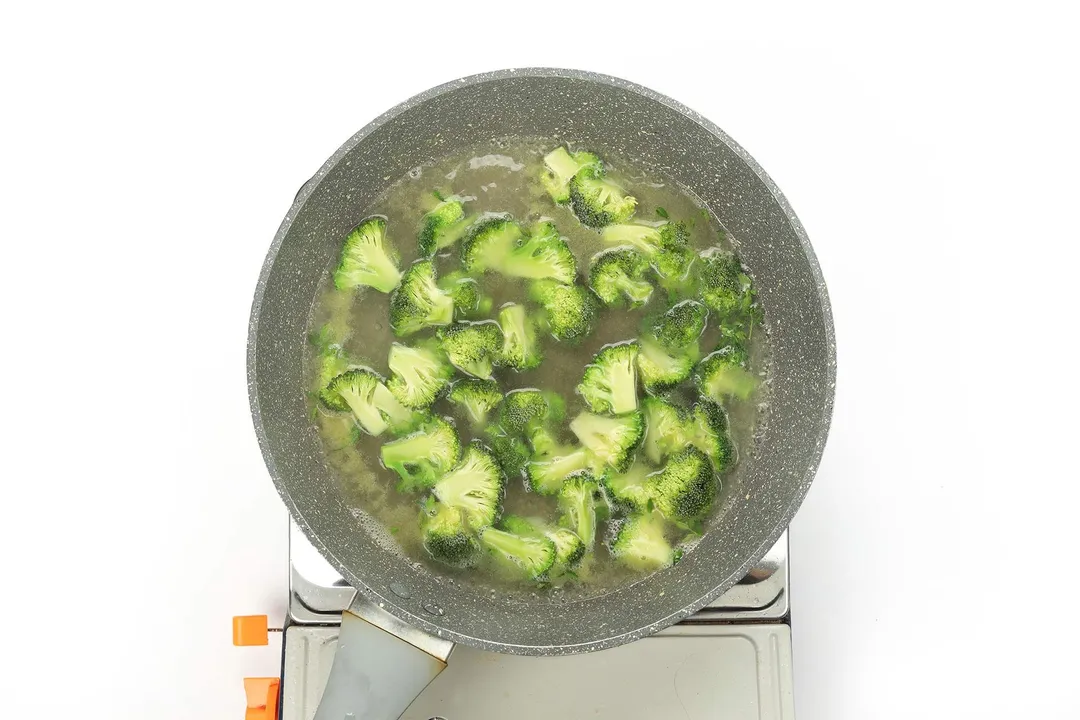 A large and deep pan filled with broccoli florets and a small amount of water