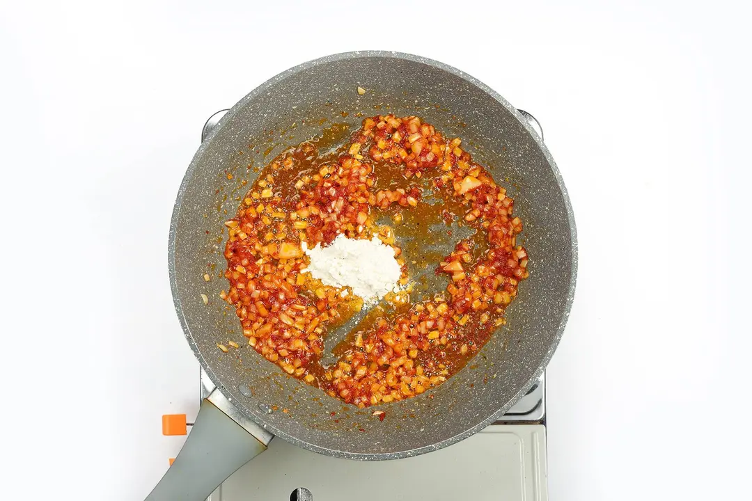 Flour being added into a pan of tomato paste and garlic