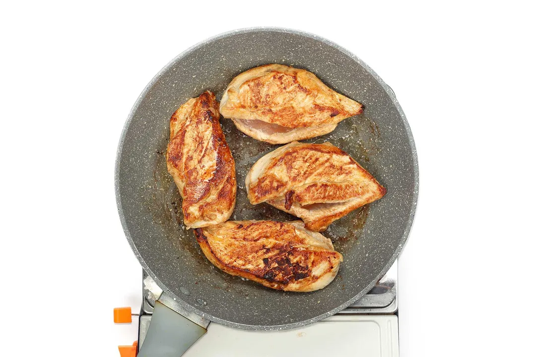 A large pan containing four pieces of chicken breast with charred meat
