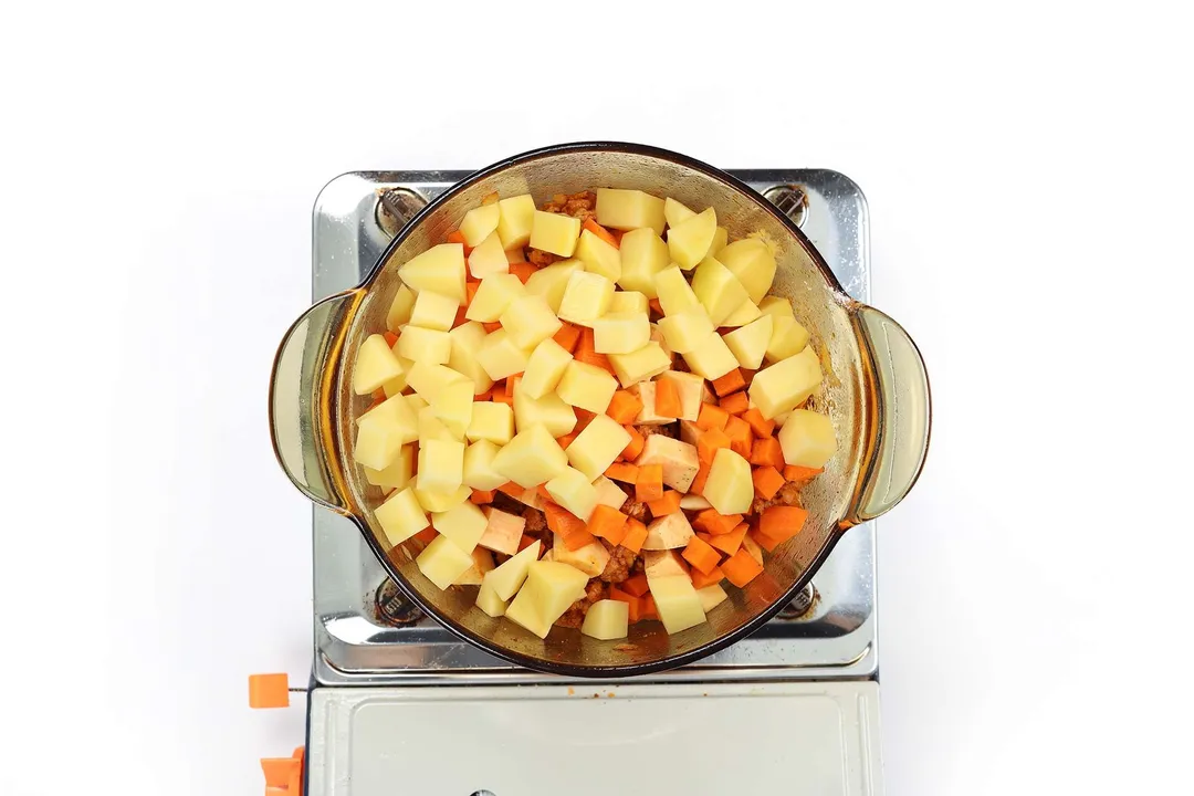 A glass saucepan cooking a lot of cubed potatoes and coarsely diced carrots