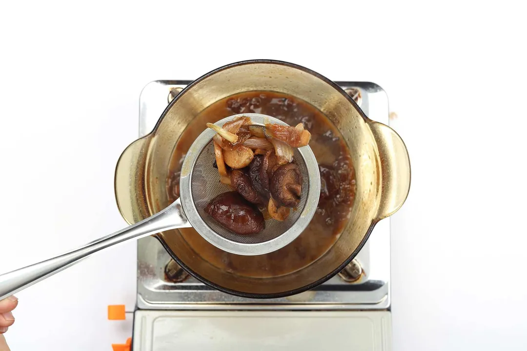 A skimmer removing dried shiitake mushrooms and garlic from a saucepan