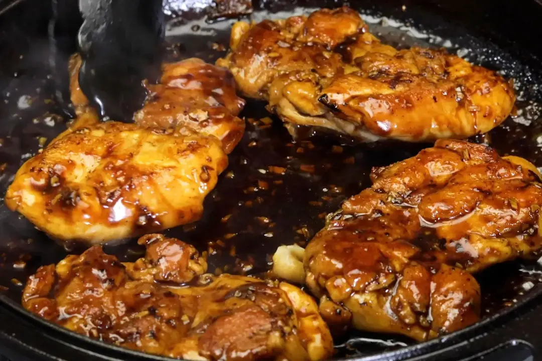 Teriyaki chicken lying in a black cast iron skillet with lots of sauce