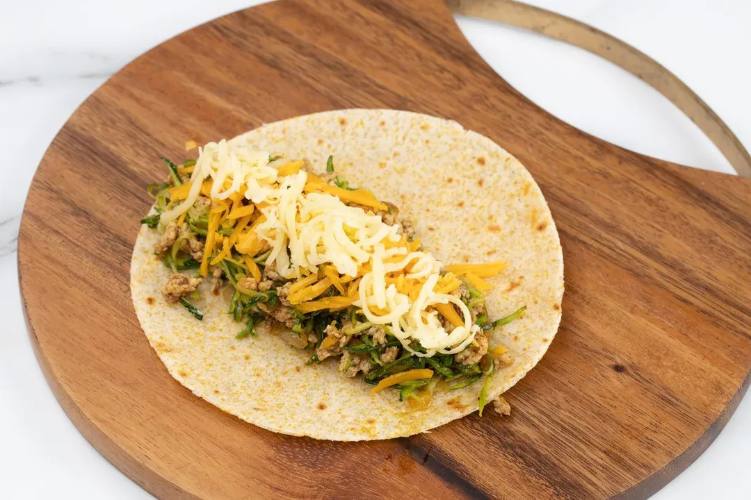 a tortilla with cheese and filling on a cutting board