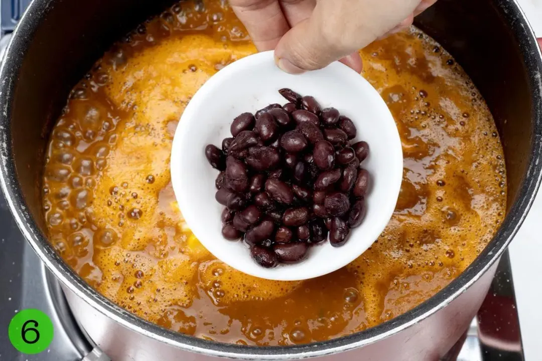 A hand putting some kidney beans into a pot of Chicken Tortilla Soup