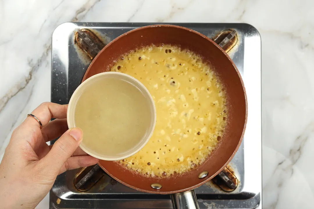 pouring chicken broth from a small bowl into a skillet of sauce