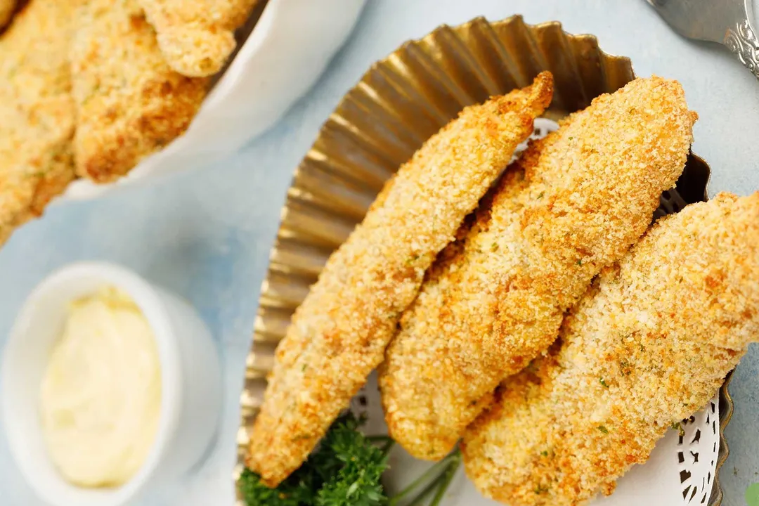 a plate of cooked chicken tender and a small bowl of mayonnaise