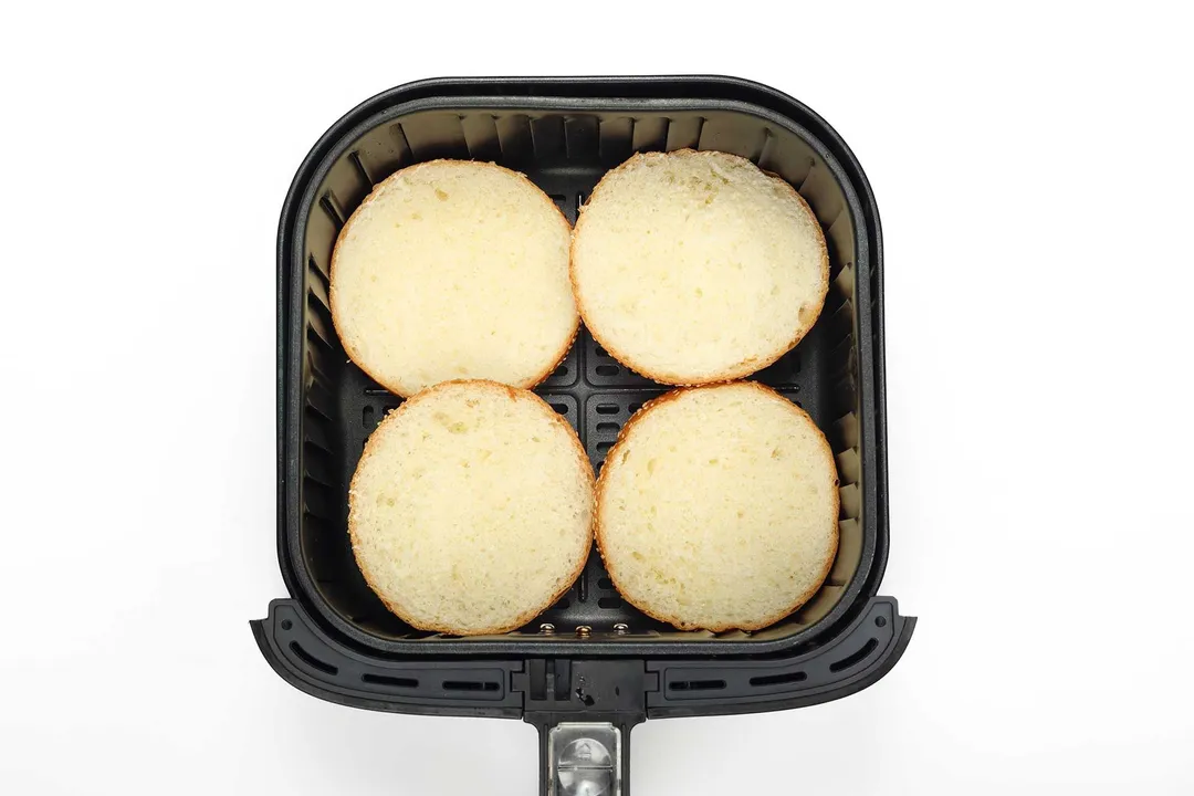 Four hamburger buns halves in an air-fryer basket