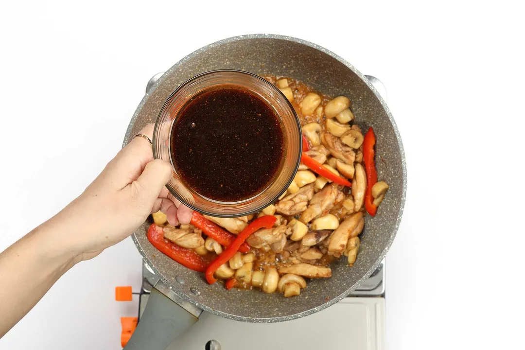 A sauce being added into a pan with chicken, mushrooms, and bell peppers