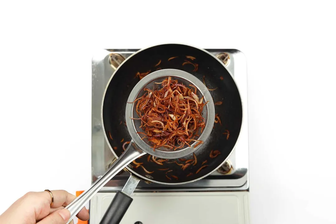 Fried shallots being removed from a pan