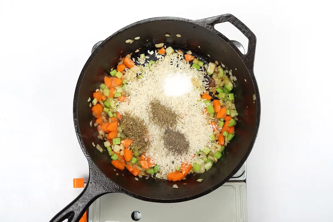 Uncooked rice, vegetables, and seasonings in a cast iron skillet