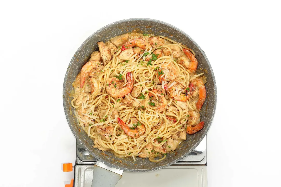 A skillet of chicken and shrimp alfredo with some chopped parsley scattered on top