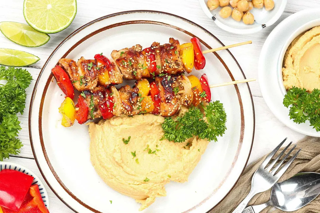 A plate of chicken skewers served with chickpea puree and decorated with parsley