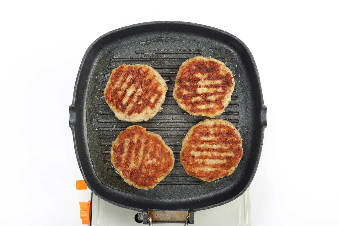 A griddle cooking four meat patties whose surfaces are charred brown