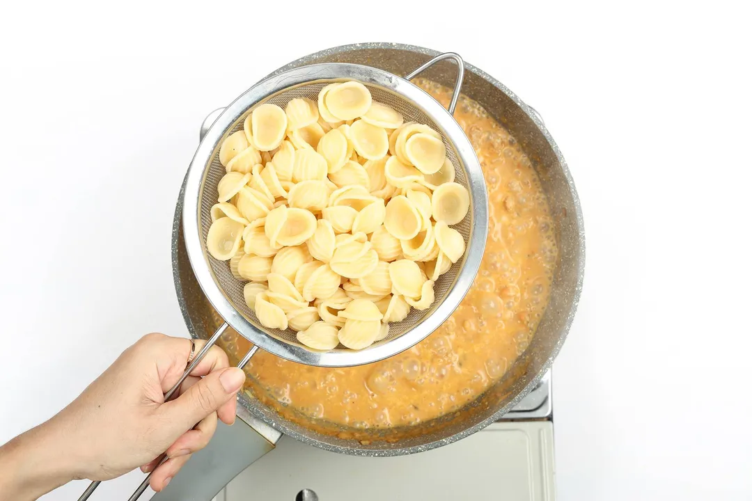 Orecchiette pasta being added to chicken and tomato sauce