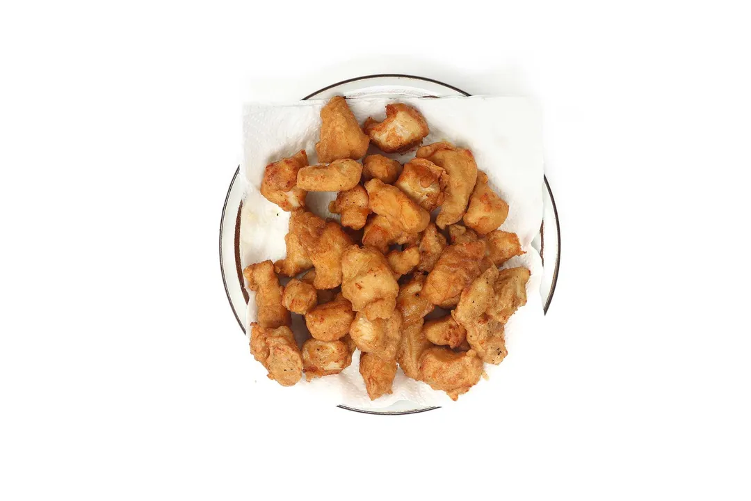 A white plate with black rim containing pieces of deep-fried chicken cubes laid on a square paper towel