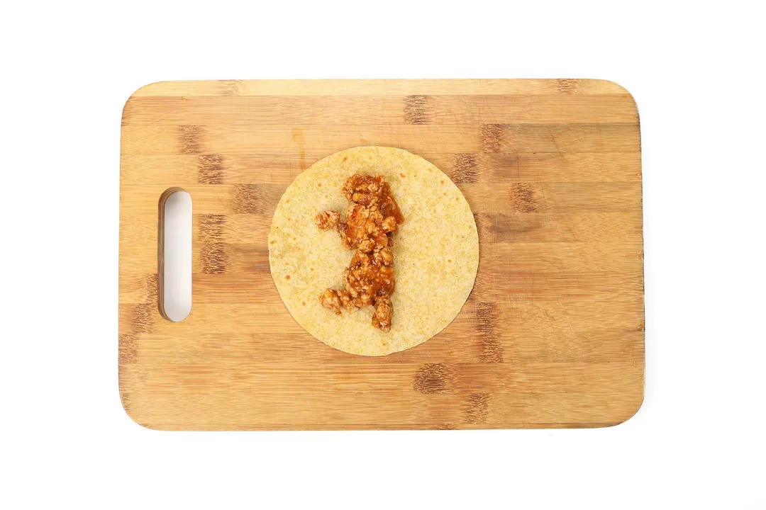 a corn tortilla with ground chicken on a cutting board