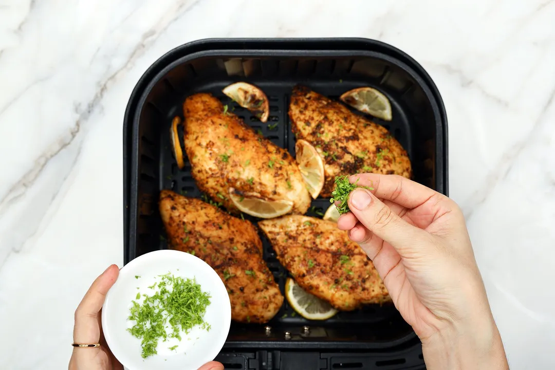 sprinkle chopped parsley from a small bowl on top of cooked chicken breast in an air fryer