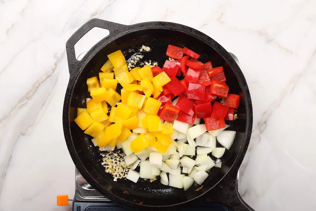 red and yellow diced bell pepper and diced onion in a skillet
