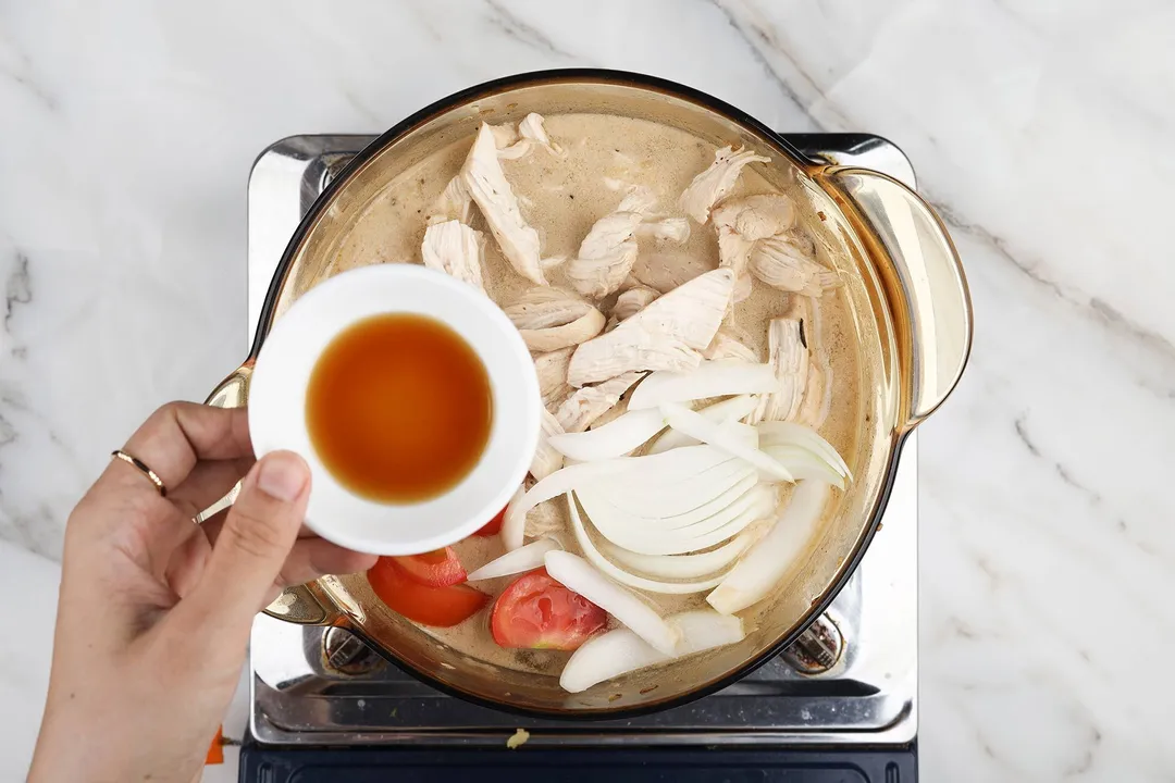 hand holds a small bowl of fish sauce on top of a pot of soup