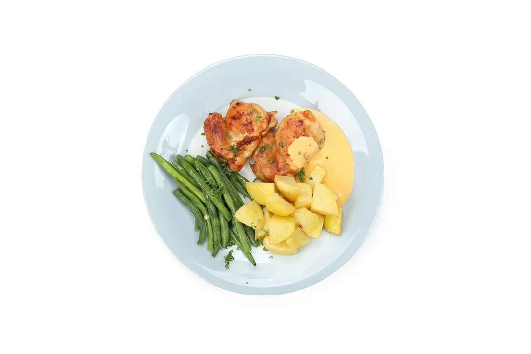 a plate of cooked chicken thighs and potato cubes, green bean