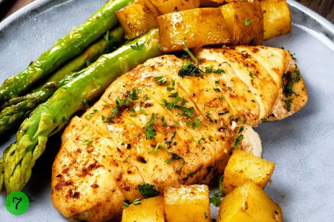A baked chicken breast, potato cubes, and asparagus laid on a plate.