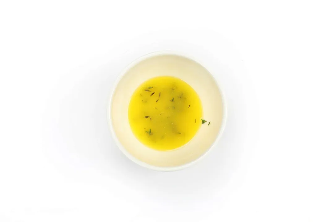A small white bowl containing melted butter and chopped parsley