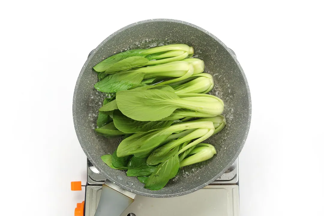 A pan cooking a lot of green bok choy in a small amount of water