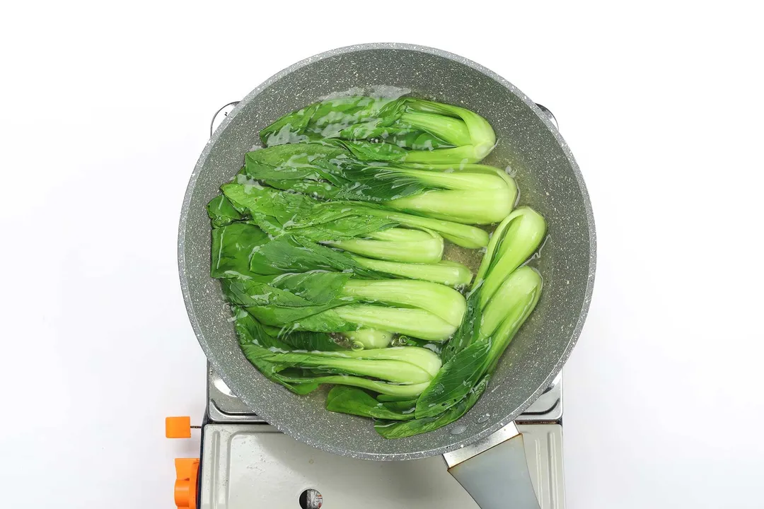 A pan cooking bright green bok choy in water